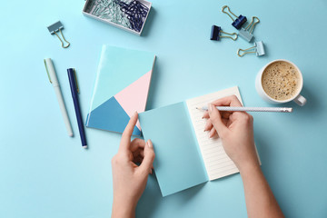Female hands with stationery and cup of coffee on color background