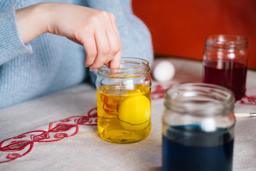 Female hand dyeing easter egg on yellow liquid. Preparation to celebrate easter, easter eggs painting.