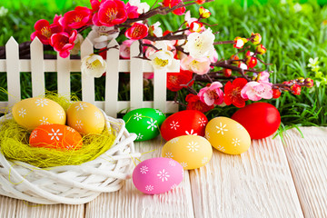 Colorful Easter eggs on white wooden table and flowers on grass