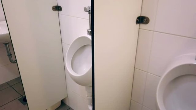Filming inside of toilet with white urinals separated with plastic walls. Public toilet with white ceramic tiles and separated male and female part.