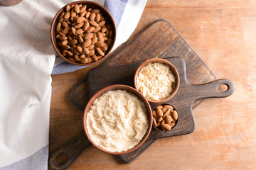 Bowls with tasty almond flour, flakes and nuts on wooden table