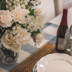 Close-up table setting. On the table are plates on napkin, bottle of wine and vase of flowers.