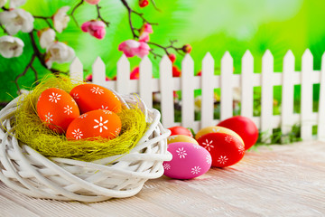 Colorful painted Easter eggs, nest and white fence on wooden table and nature background