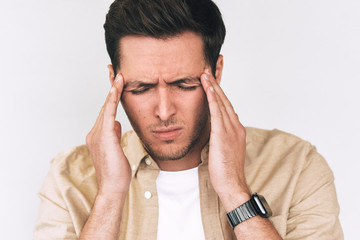 Closeup portrait of sad Caucasian young man standing with closed eyes holding hands on head looking stressful. Stressed man suffering from headache. People, health, tension and migraine concept