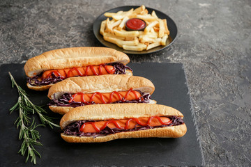 Slate plate with tasty hot dogs on dark table