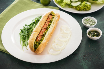 Plate with tasty hot dog on color table