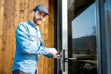 Workman repairing entrance door lock of the modern house or hotel during the sunny weather outdoors