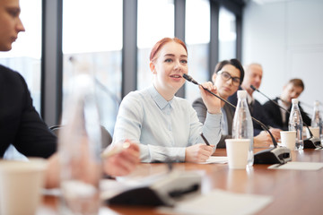 Portrait of smiling young businesswoman speaking to microphone during press conference or training...