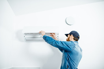 Repairman in blue workwear serving the air conditioner changing filter on the white wall background