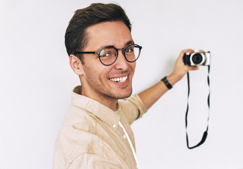 Cheerful happy freelancer young man taking selfie over white studio background and looking to the camera. Young male smiling and wearing eyewear making self portrait and blogging using digital camera.