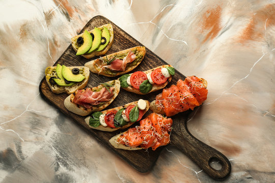 Wooden board with fresh tasty bruschettas on color background