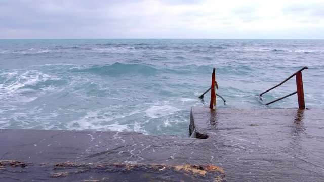 Stairs going into rough sea. Bad day at the beach with big waves.