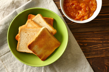 Bowl with tasty toasted bread and jam on wooden table