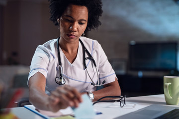 Female black doctor working at desk in doctor's office.