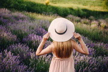 Fototapeta premium Pregnant girl blonde in a beige dress and straw hat. Lavender field. In anticipation of a child. The idea of a photo shoot. Walk at sunset. Future mom.