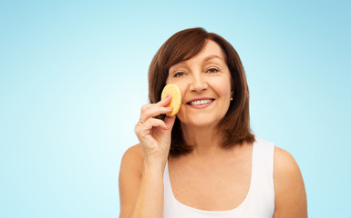 beauty, skin care and old people concept - smiling senior woman cleaning her face with exfoliating sponge over blue background