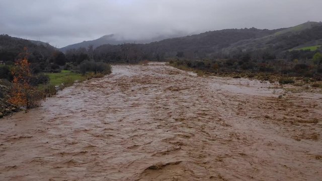 Aerial of flood waters moving fast down the Ventura River in California with runoff during winter weather flooding.