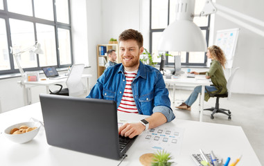 Fototapeta premium business, technology and people concept - happy smiling creative man with laptop computer working on user interface design at office