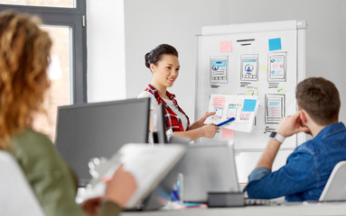 business, technology and people concept - woman showing user interface design on flip chart to creative team at office presentation