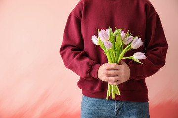 Young man with bouquet of flowers on color background. 8 March celebration