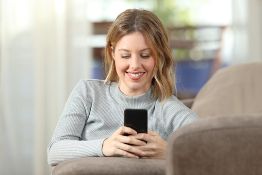 Happy lady texting on phone on a couch at home