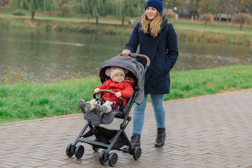 A woman walks in the park with a stroller and a small child near the lake.