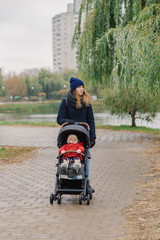 A woman walks in the park with a stroller and a small child near the lake.