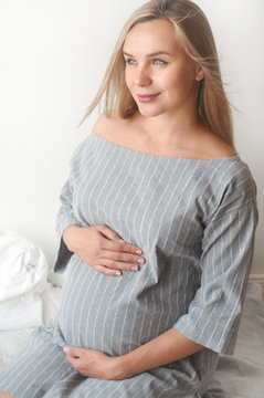 Happy pregnant woman sit on a bed at home and looking to the camera