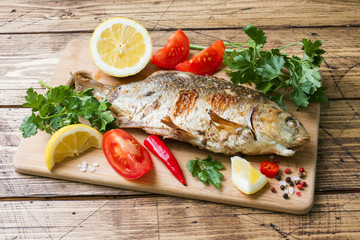 Baked carp fish with vegetables and spices on a wooden table.
