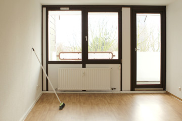 Broom stands on the floor against the wall in the middle of an empty bright room