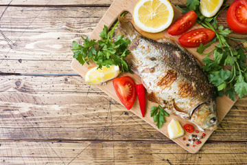 Baked carp fish with vegetables and spices on a wooden table with a copy of the space.