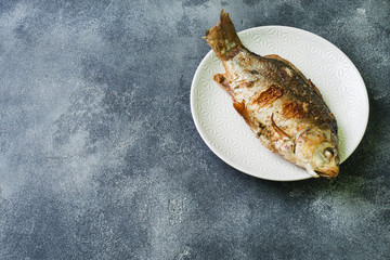 Baked carp fish on a plate. dark background. Copy space.