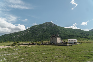 Fototapeta na wymiar Old church with a cemetery in the middle of a green meadow with a mountain in the background