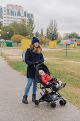 A woman walks in the park with a stroller and a small child near the lake.