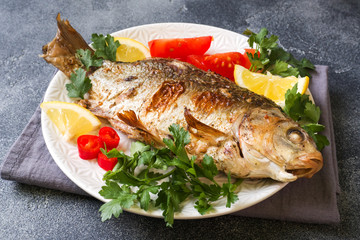 Baked carp fish with vegetables and spices on a plate on a dark table with a copy of space.