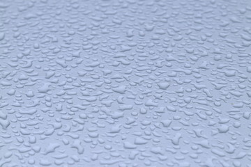 View of the big raindrops on the roof of a light blue car