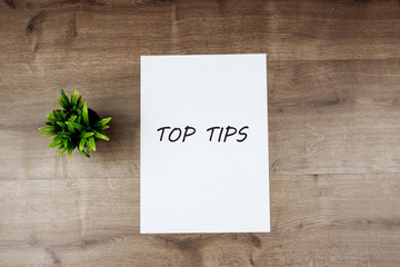 Text TOP TIPS on white paper and flower on wooden background