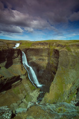 The Haifoss Waterfall with golden clouds in the sky. The flowing water is captured by a long...