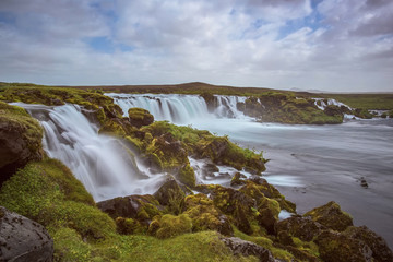 The Hólmsárfoss Waterfall with golden clouds in the sky. The flowing water is captured by a long...