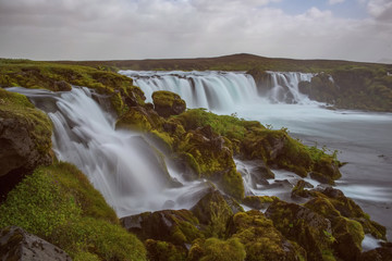 The Hólmsárfoss Waterfall with golden clouds in the sky. The flowing water is captured by a long exposure. Amazing blue color of water from the glacier. Natural and colorful environment...