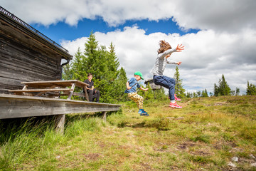 Summer nature side view of children in mid air jumping of a porch landing on grass hill.