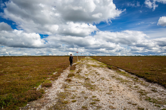 A young male walking alone at a flat highland hiking trail. Scenic landscape view with beautiful clouds.