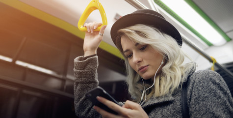 Happy female passenger listening to music on a smartphone in public transportation.