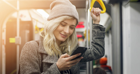Happy female passenger listening to music on a smartphone in public transportation.