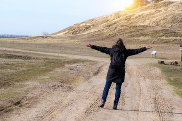 Europ&auml;ische Frau in einer schwarzen Jacke hebt die Arme auf leerer Stra&szlig;e in Richtung zum Sonnenuntergang an