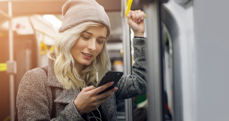 Happy female passenger listening to music on a smartphone in public transportation.