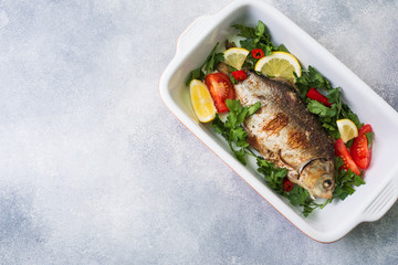 Baked carp fish with vegetables and spices in a baking tray with copy space.