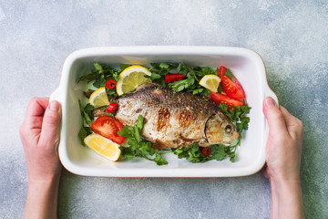 Baked carp fish with vegetables and spices in a baking tray with copy space.