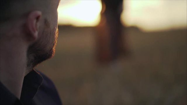 Handsome guy trying to get acquainted with russian girl outdoors. The girl approaches the guy in the sunset. The guy is sitting at a haystack, and a girl in a black dress approaches him. The guy looks