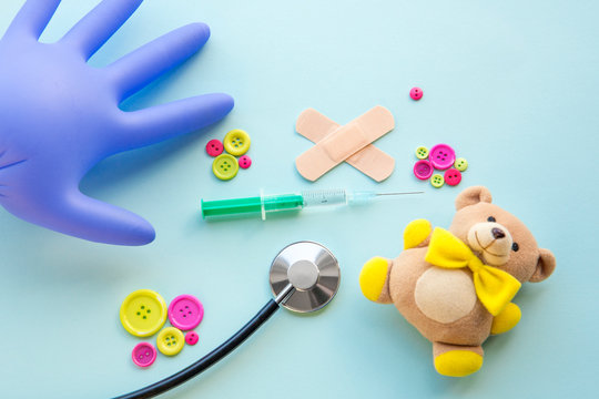 Children vaccination concept. Syringe surrounded with different medical tools and children toys, blue background, flat lay view.